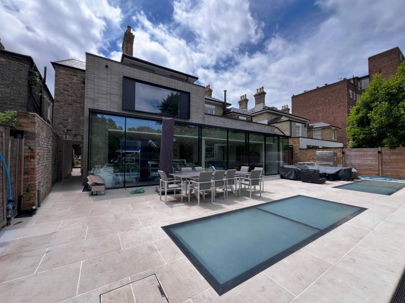 Rear extension with frameless glazing and a stone terrace in Putney