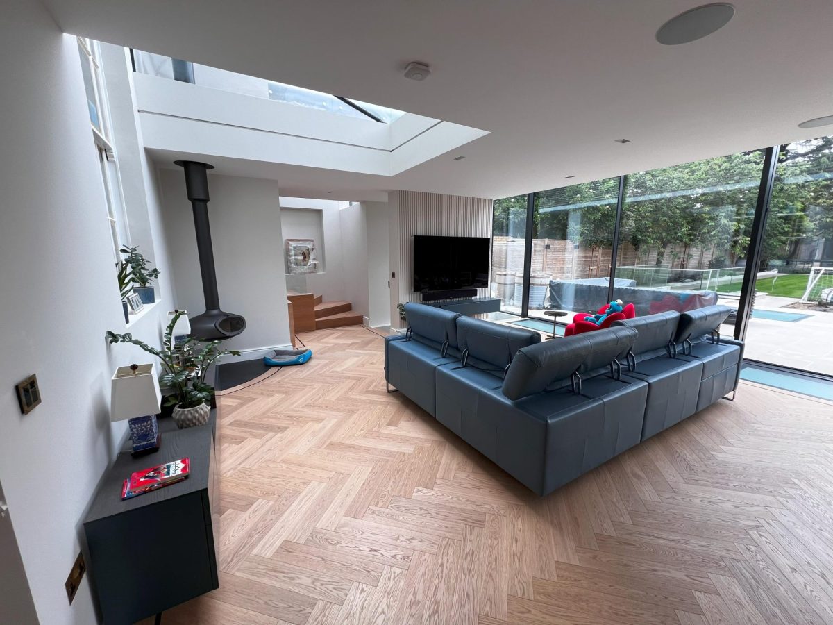 Open-plan living room with herringbone floor, rooflight and frameless glazing