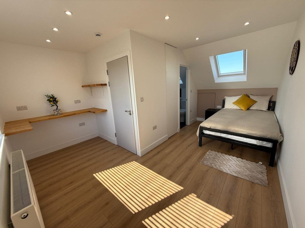 Converted loft bedroom with rooflight, oak desk and en-suite door in Chessington