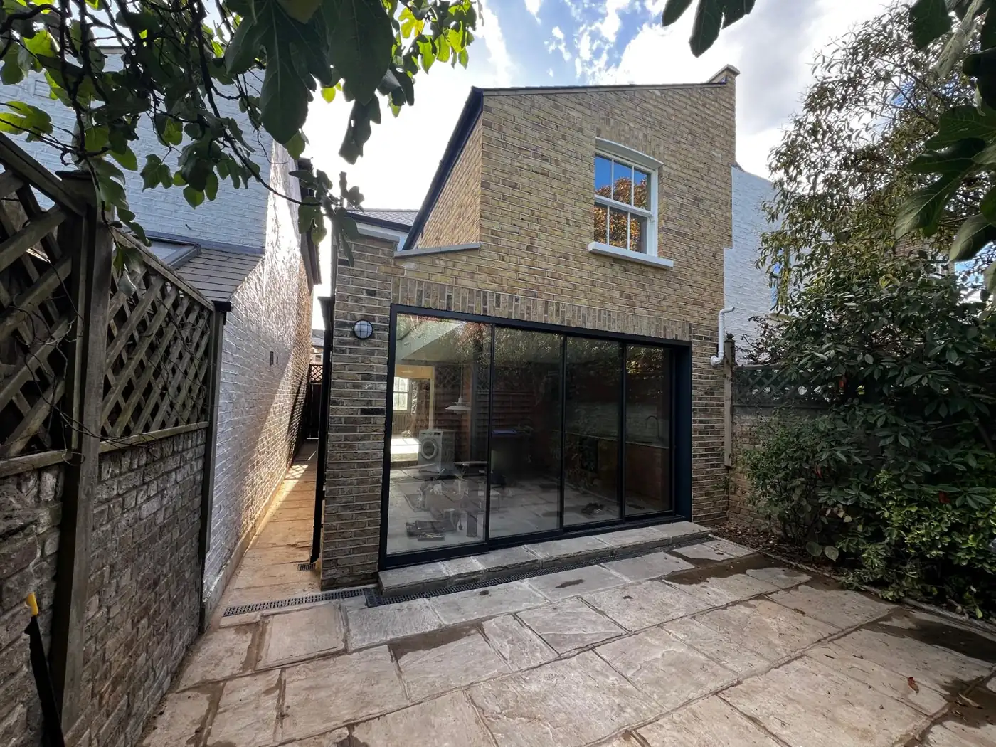 Brick extension with slim black-framed sliding doors opening onto a paved garden, Denmark Road, Wimbledon
